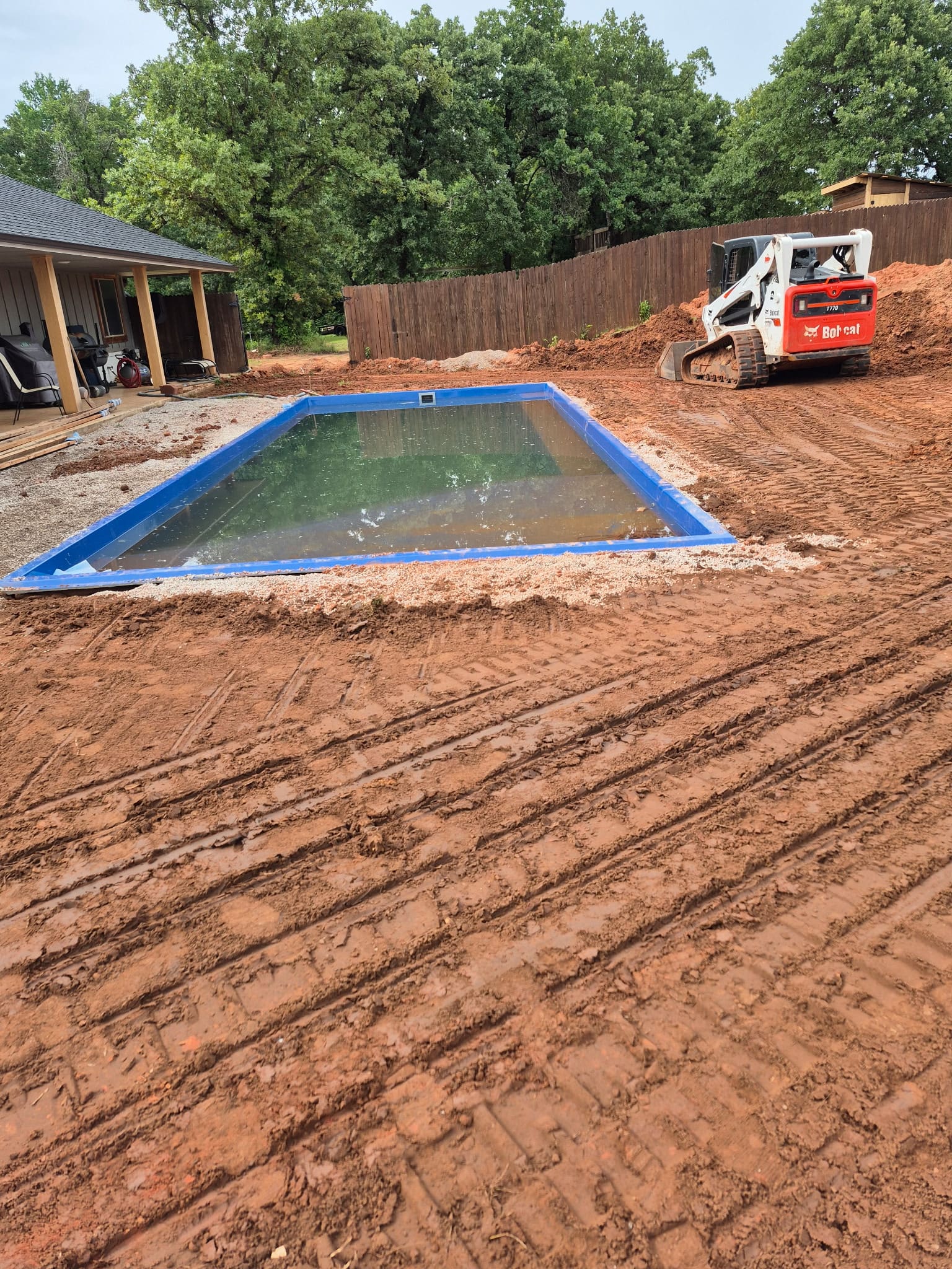Residential backyard pool installation with excavator and muddy construction site