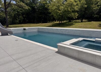 Modern rectangular inground pool and spa with gray tile deck and slide