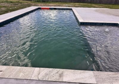 Residential rectangular backyard pool with greenish water and concrete deck