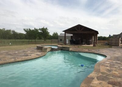 backyard freeform swimming pool with spa, stone decking, and covered patio