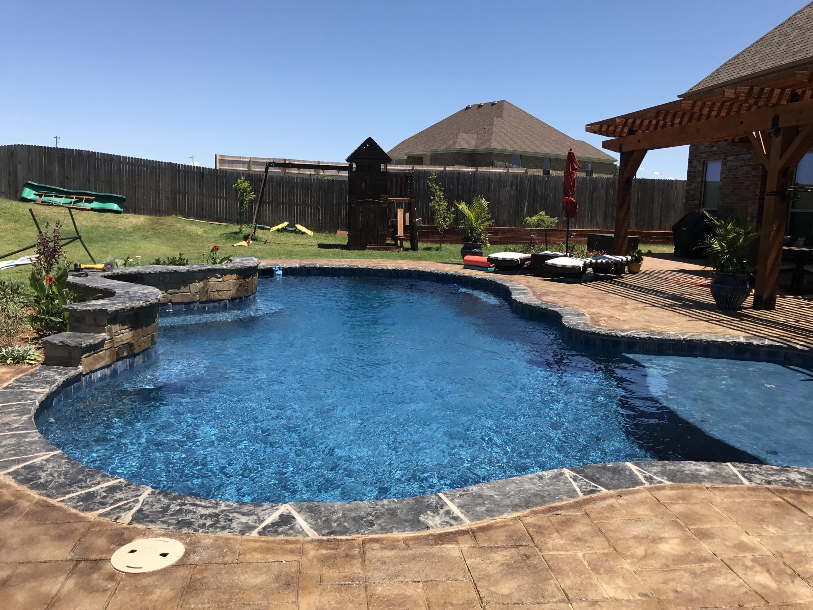 Backyard custom gunite pool with pergola, stone coping, and lounge area