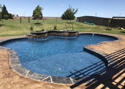Backyard freeform blue swimming pool with stamped concrete patio and water feature
