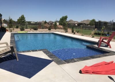 backyard inground pool with blue spa tile and red patio chair