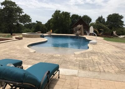 Curved backyard pool with spa, slide, lounge chairs, and patio stones