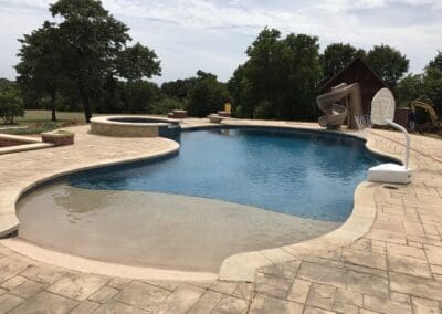 Residential freeform pool with tanning shelf, spa, slide, and basketball hoop