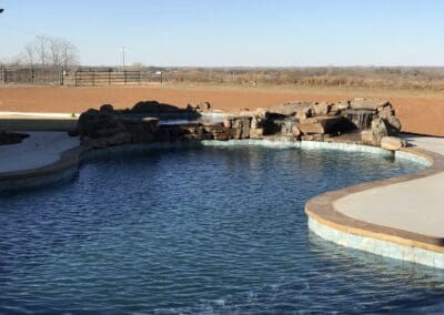 Backyard freeform swimming pool with rock waterfall and concrete decking