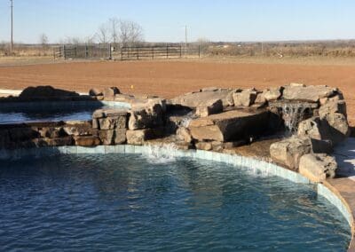 Pool with rock waterfall feature and rural field beyond