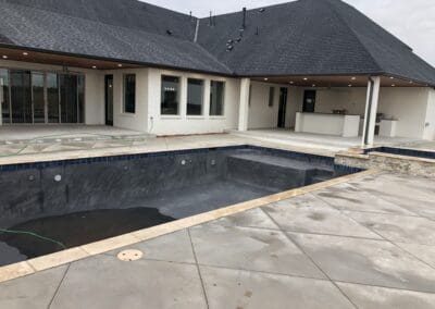 Backyard modern home with unfinished in-ground pool and wet concrete patio