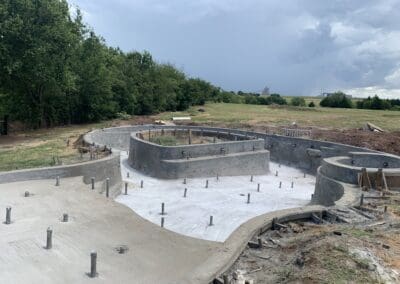 Residential concrete pool shell under construction on grassy backyard with trees