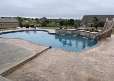 Backyard freeform pool with stone water feature and slide, concrete decking