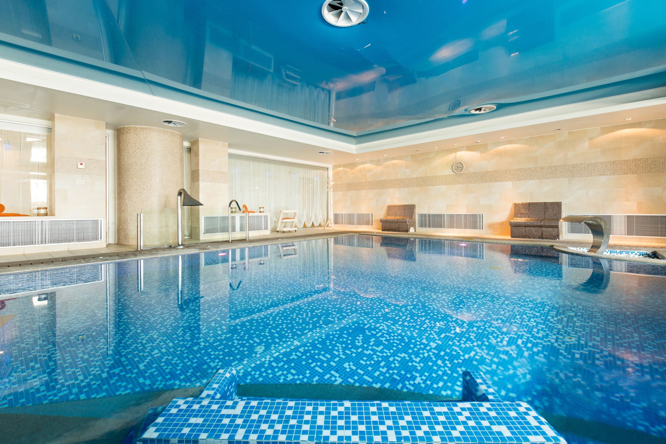 Indoor commercial pool with blue mosaic tile and lounge seating