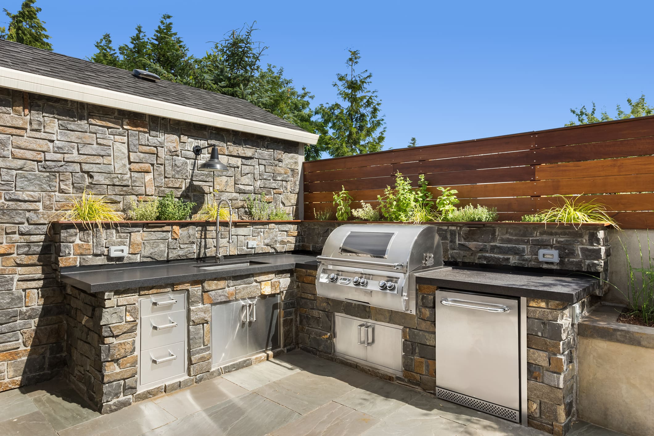 Outdoor kitchen with stone hardscape, stainless grill, countertops, and planter
