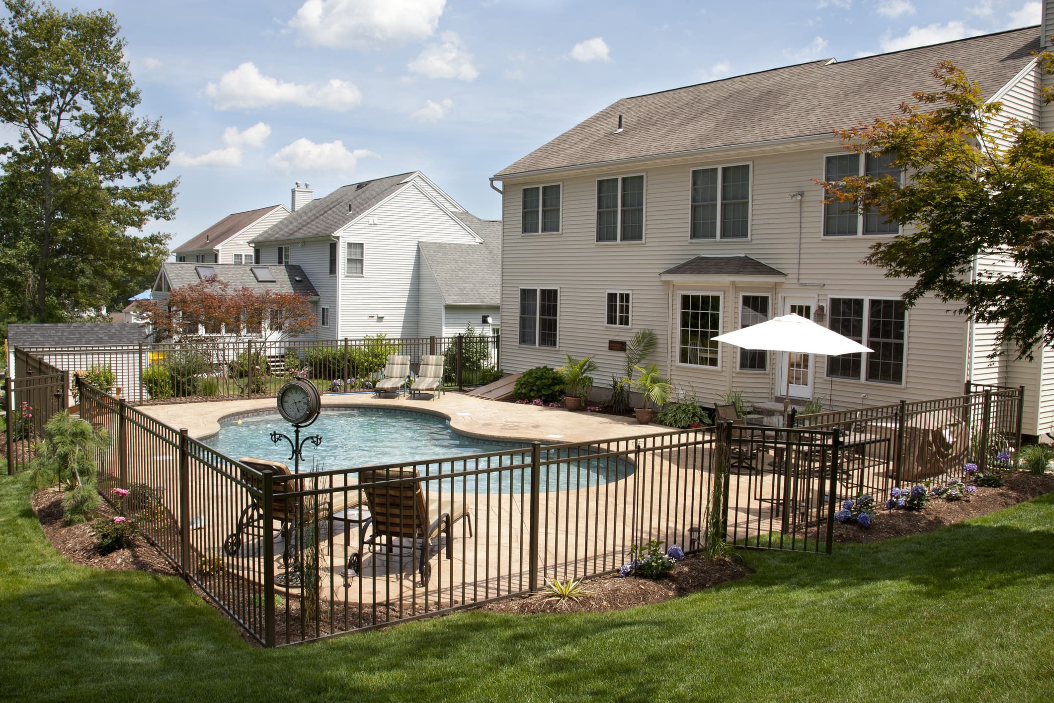 Backyard pool patio with safety fence, lounge chairs, umbrella, and landscaping