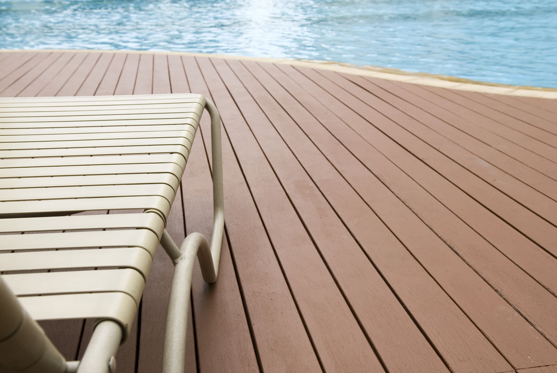 Poolside composite decking with lounge chair beside shimmering water